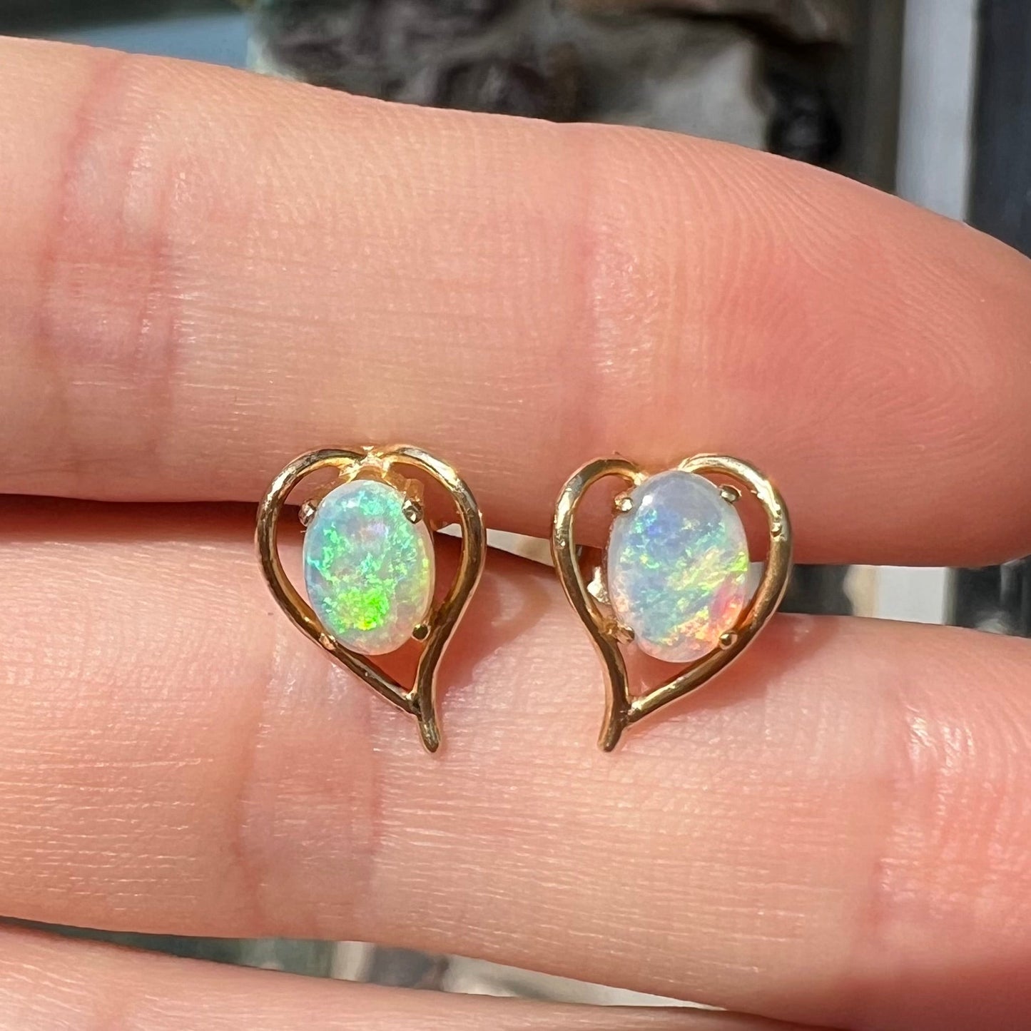 A pair of yellow gold, heart shaped stud earrings set with oval cabochon cut natural opal stones.