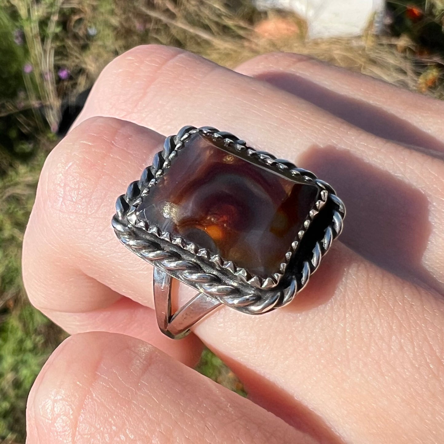 Rectangle cut fire agate ring with silver rope design and split shank, worn at an angle on a finger in natural light.