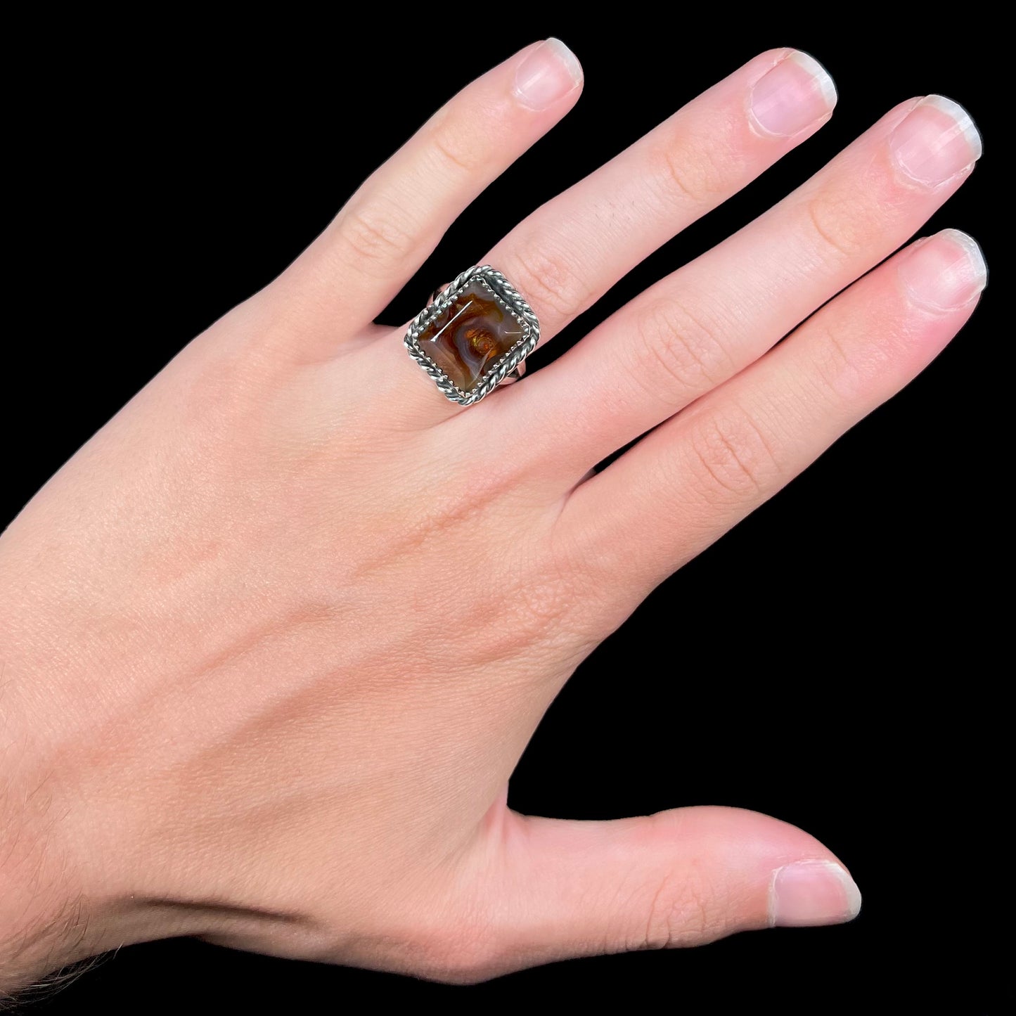 Hand wearing a rectangle cut fire agate ring made from sterling silver against a black background.
