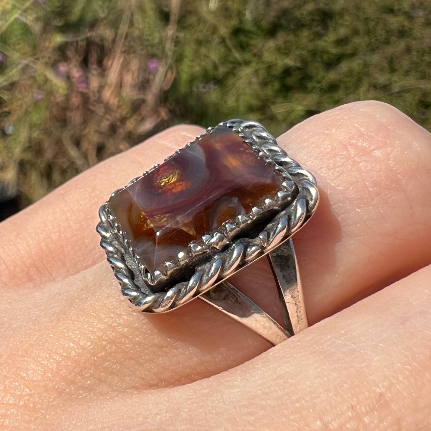Angled view of rectangle shaped fire agate ring in the sunlight, worn at an angle showing silver rope design.