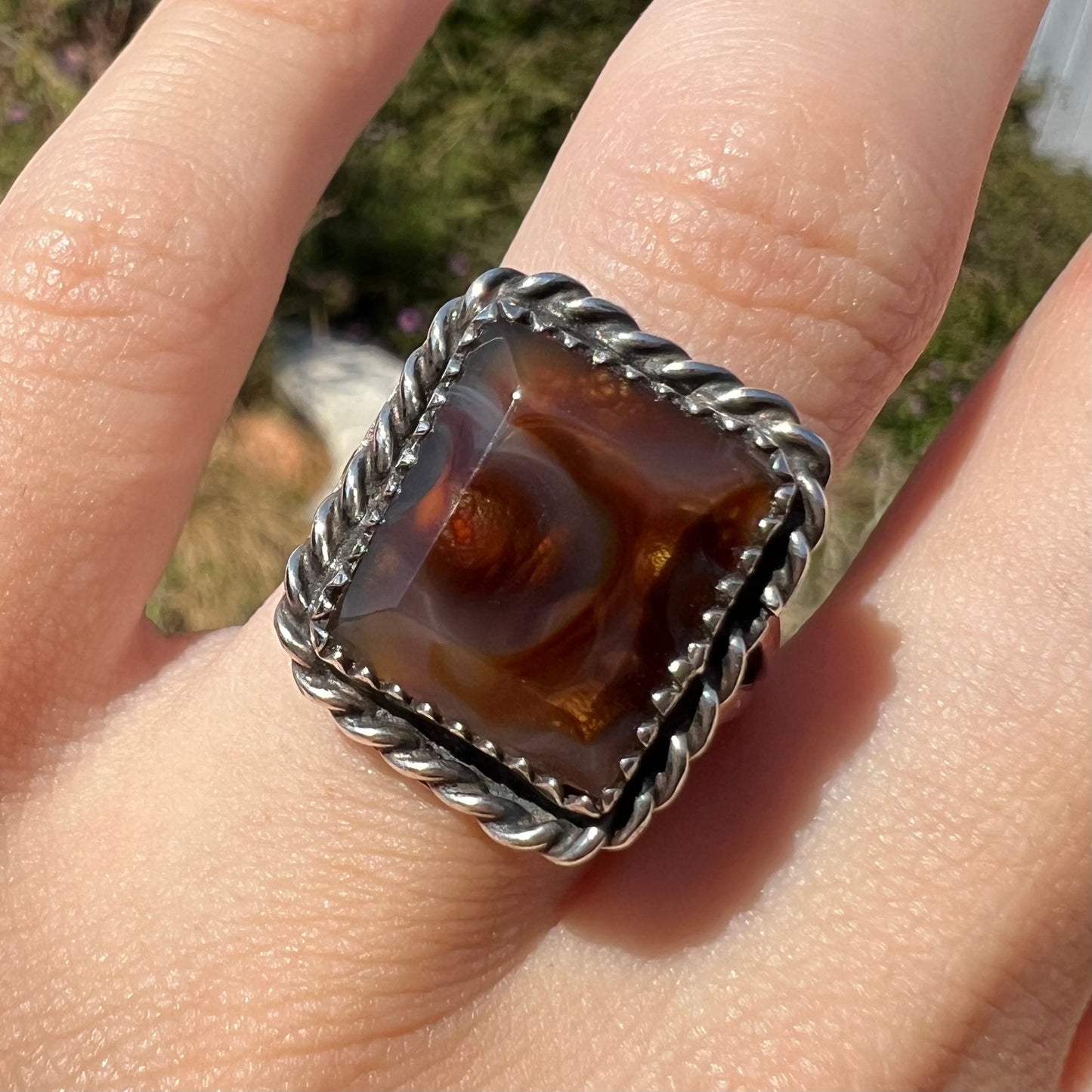 Front facing close-up of silver rectangle cut fire agate ring in the sunlight, worn on a finger.