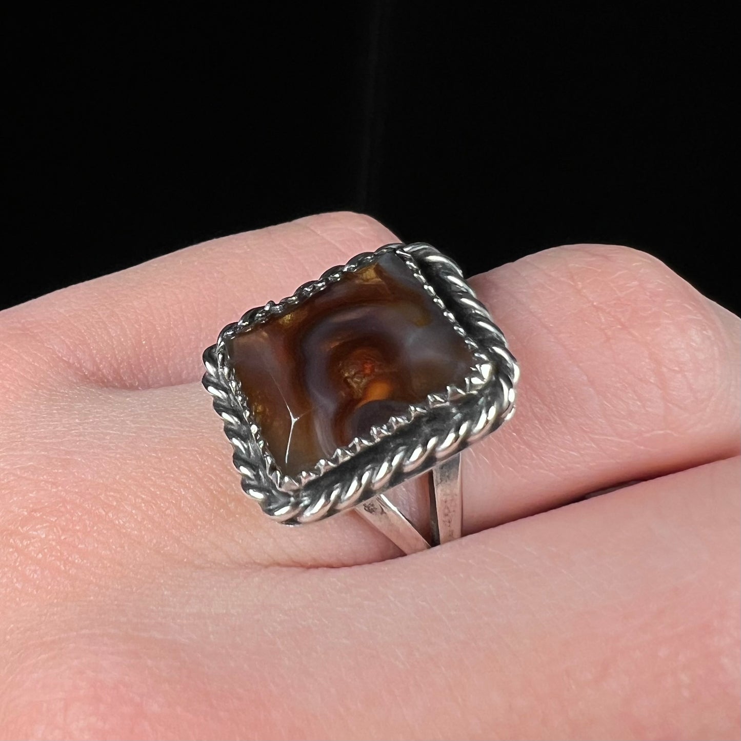 Rectangular shaped fire agate ring worn on a finger, shown at an angle against a black background.
