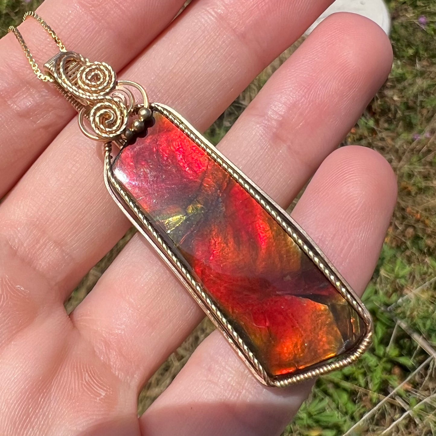 Angled natural light view of a red ammolite necklace held in a hand.