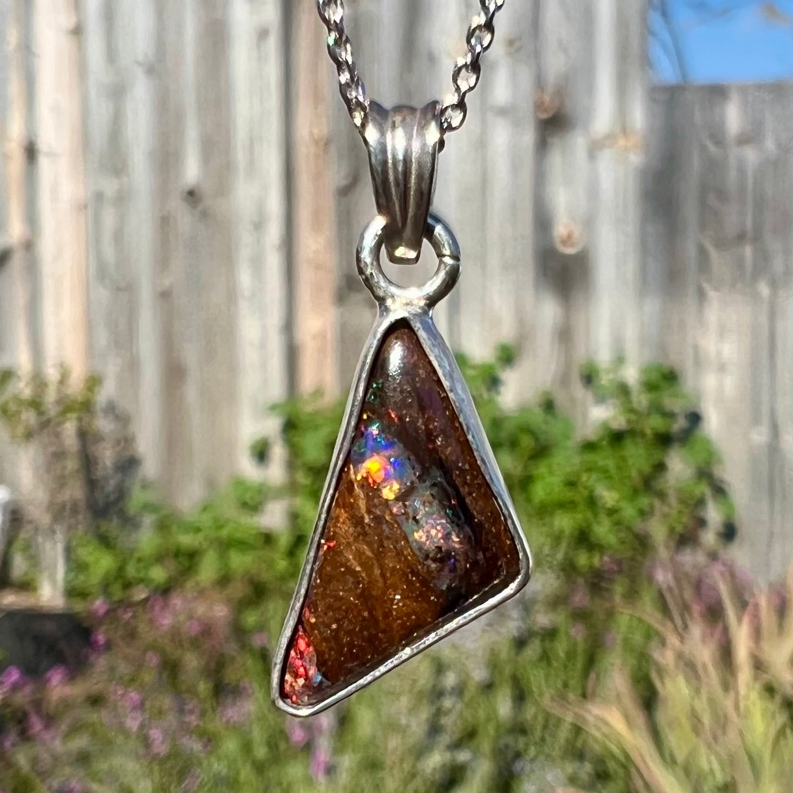 A sterling silver necklace bezel set with a triangle shaped boulder opal.  The opal has red and blue flashes.