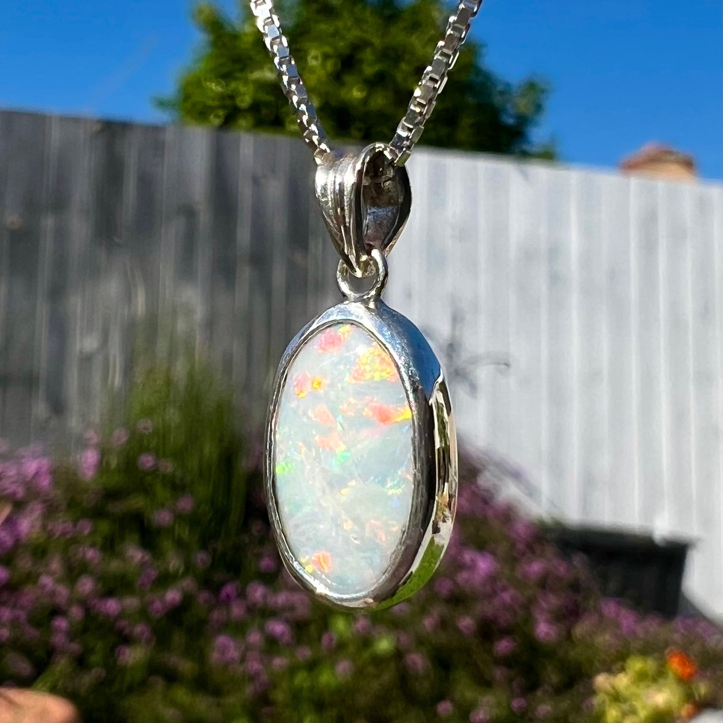A ladies' sterling silver necklace bezel set with a natural white crystal opal. The opal has red and blue fire.