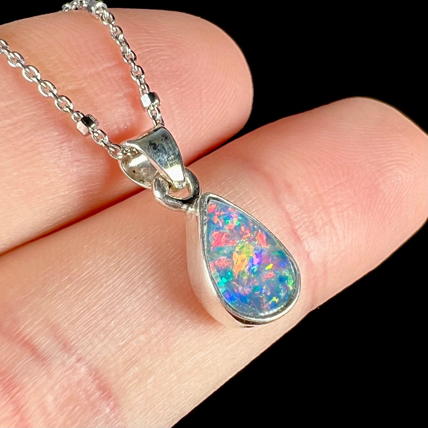 A pear shaped black opal necklace set in sterling silver. The opal vividly flashes every color of the rainbow.
