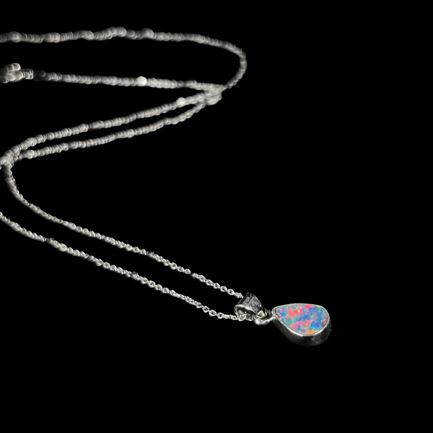 A pear shaped black opal necklace set in sterling silver. The opal vividly flashes every color of the rainbow.