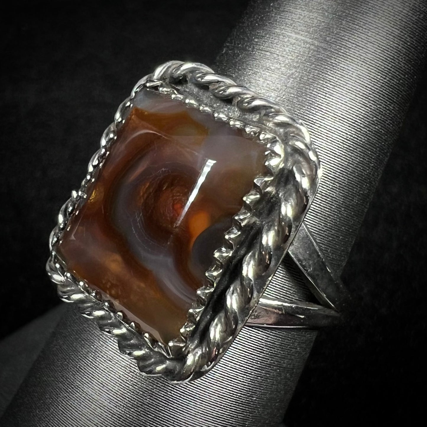 A silver rope design fire agate ring with a split shank shown from an angle.