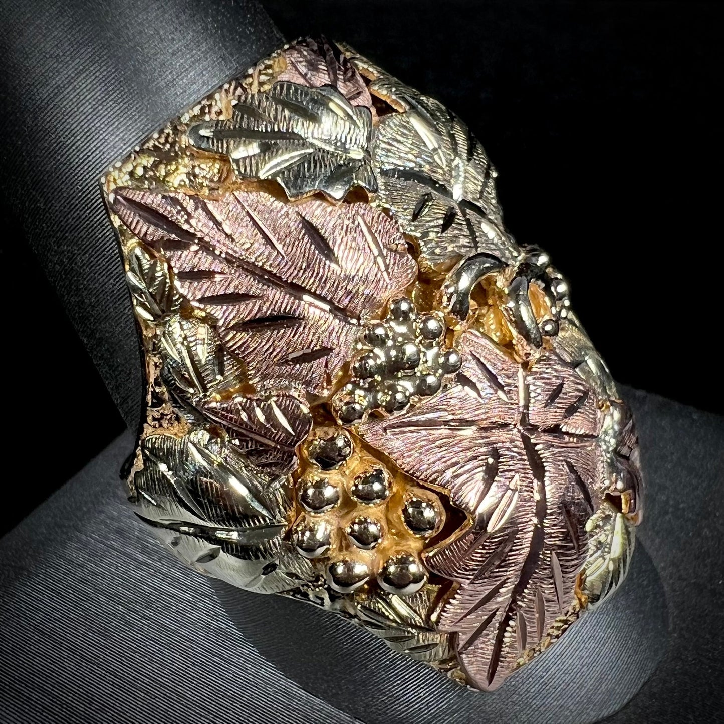 A men's solid gold ring. The ring is Black Hills gold featuring a grapevine and leaf motif with rose and green gold designs.