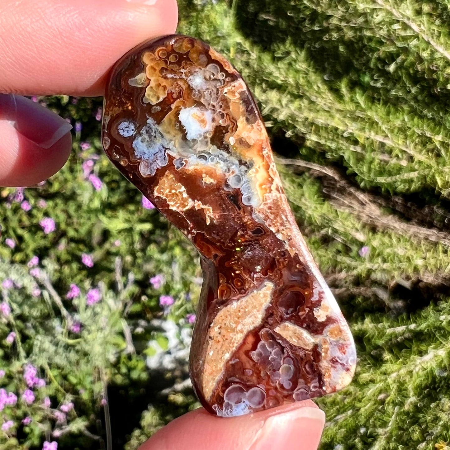 A loose, freeform cabochon cut fire agate gemstone. The stone exhibits a bubbly pattern.