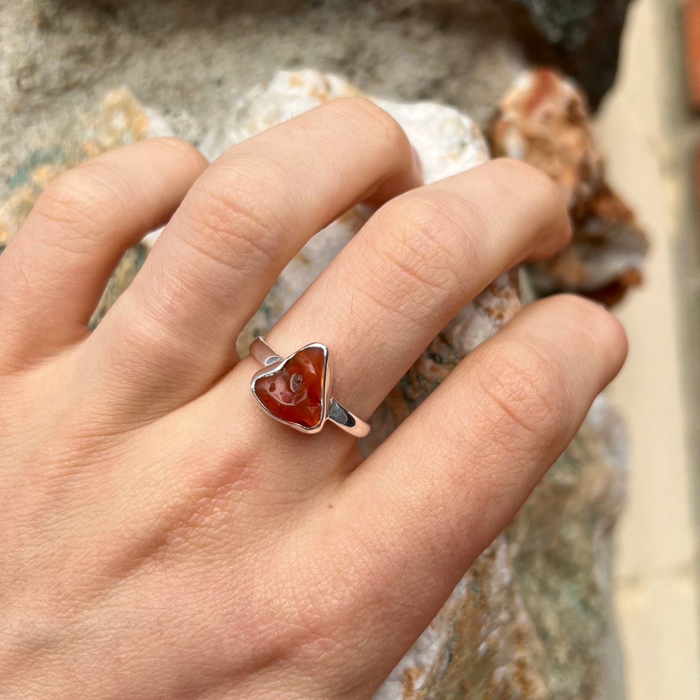 A polished fire opal crystal bezel set into a sterling silver ring. The opal is an orange color.