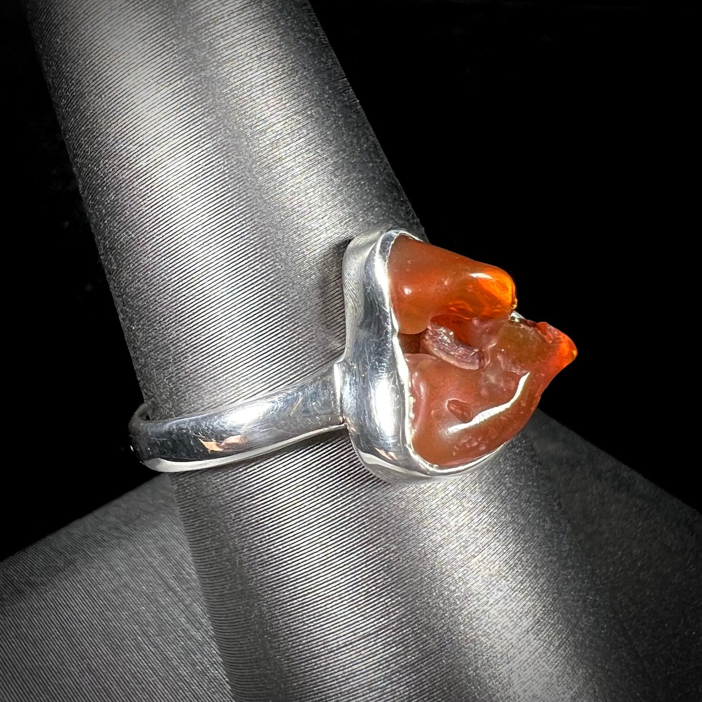 A polished fire opal crystal bezel set into a sterling silver ring. The opal is an orange color.