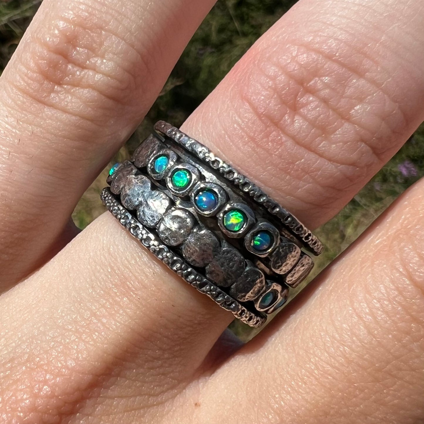 Close-up front view of an opal spinner ring set with round opals, worn on a finger in the sunlight.