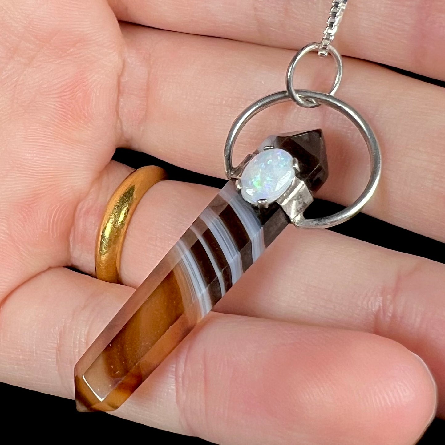 A sardonyx crystal necklace with a white opal accent, held against black background in a hand.