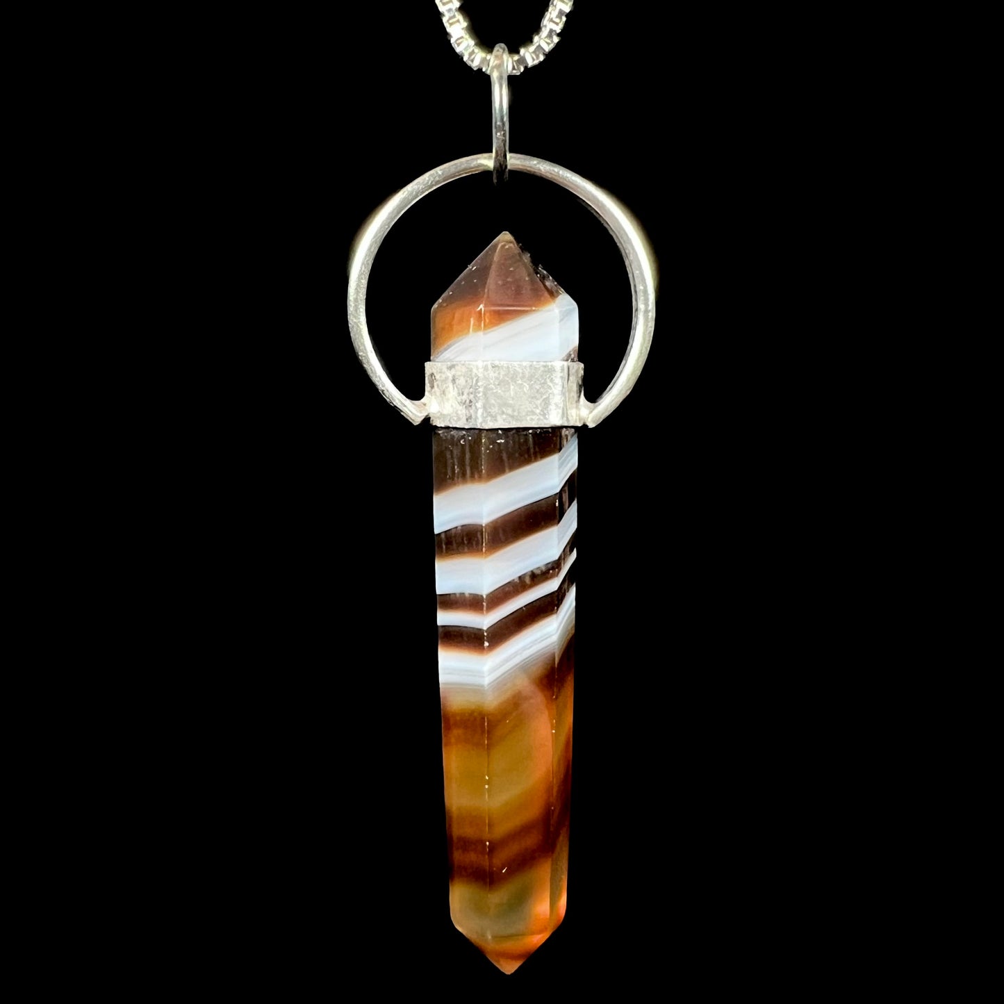 Back view of a sardonyx crystal pendant against a black background.