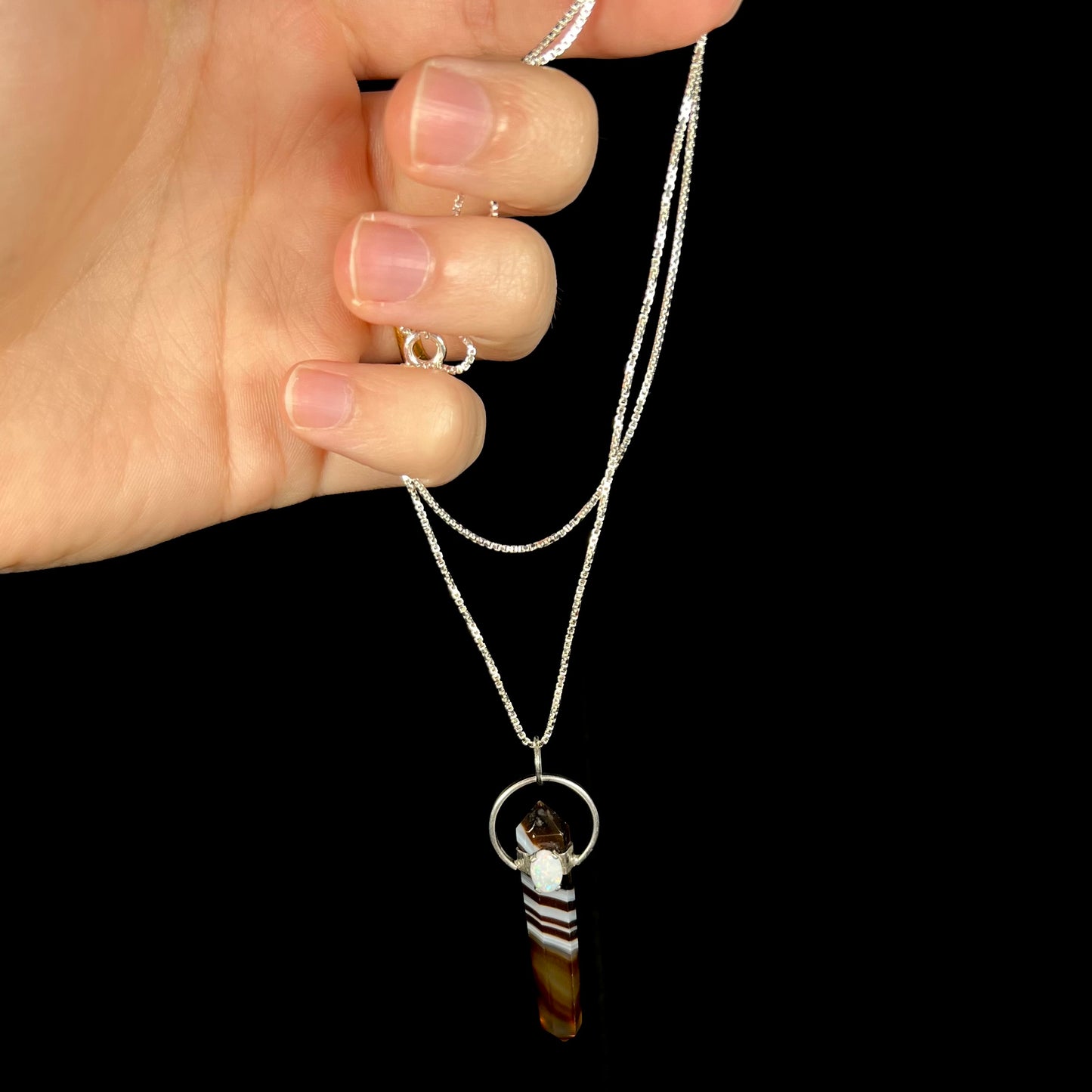 A sardonyx and opal necklace made from sterling silver, held by the chain from a hand.