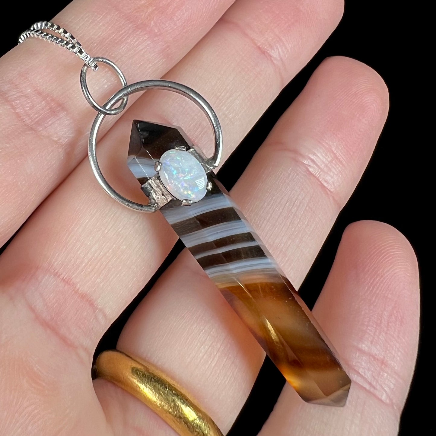 A sardonyx and opal pendant in sterling silver, held in a hand against black background.