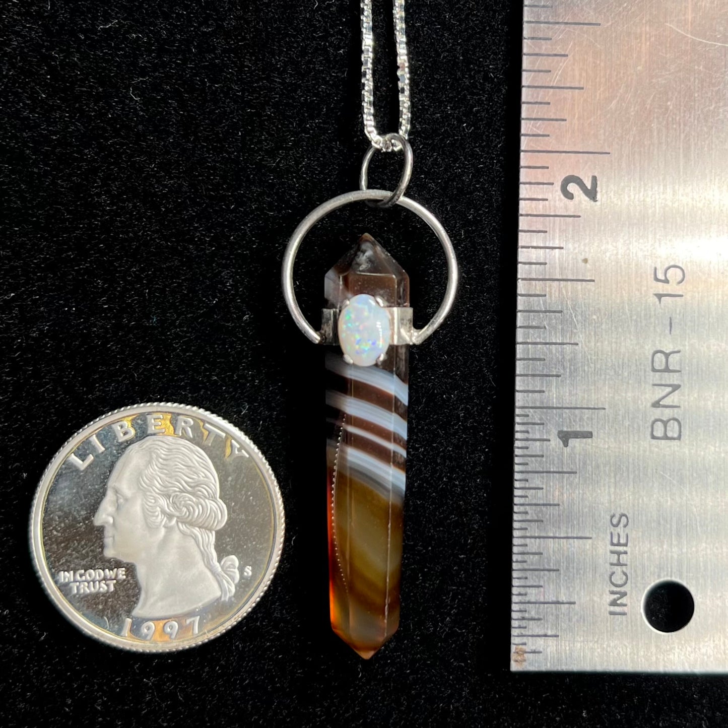 A sardonyx pendulum pendant next to a quarter coin and ruler for scale.