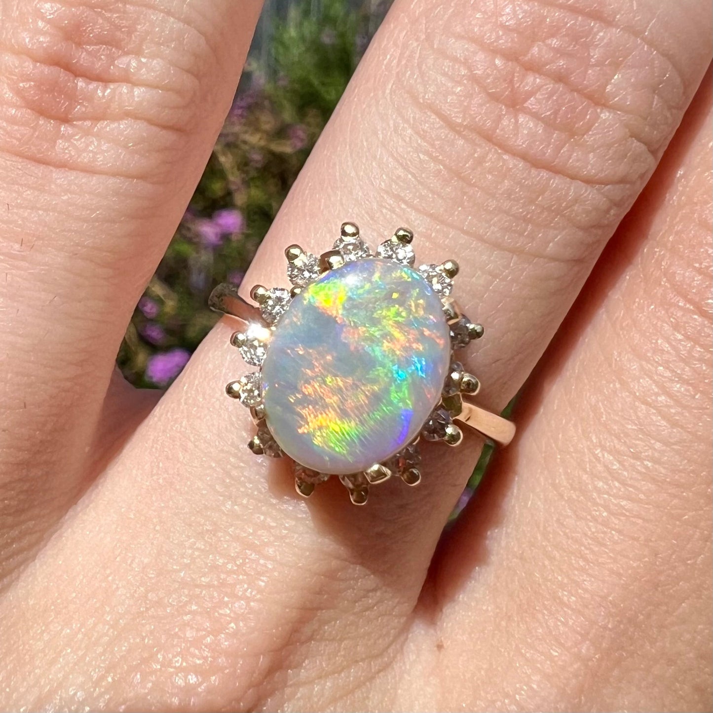 A yellow gold ring mounted with a Mintabie semi-black opal. The opal is surrounded by round diamonds.