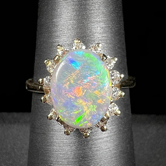 A yellow gold ring mounted with a Mintabie semi-black opal.  The opal is surrounded by round diamonds.