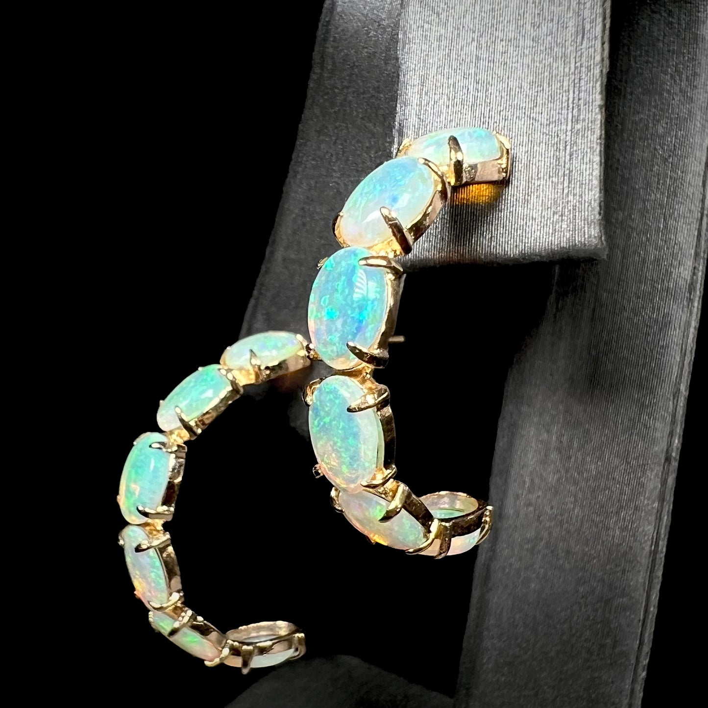 Angled macro shot of gold opal semi-hoop earrings showing subtle blue fire in the opals.