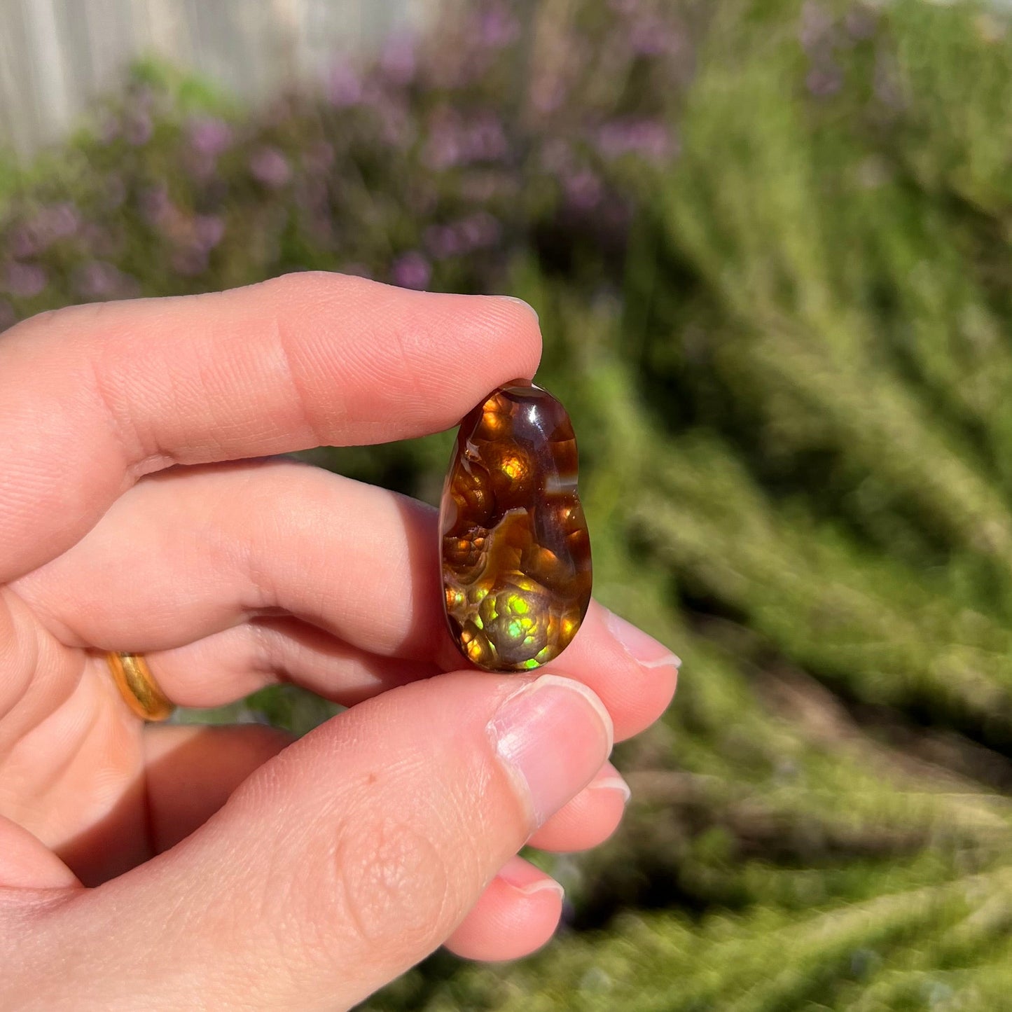 A loose fire agate cabochon. The stone has iridescent green, yellow, and blue colors.