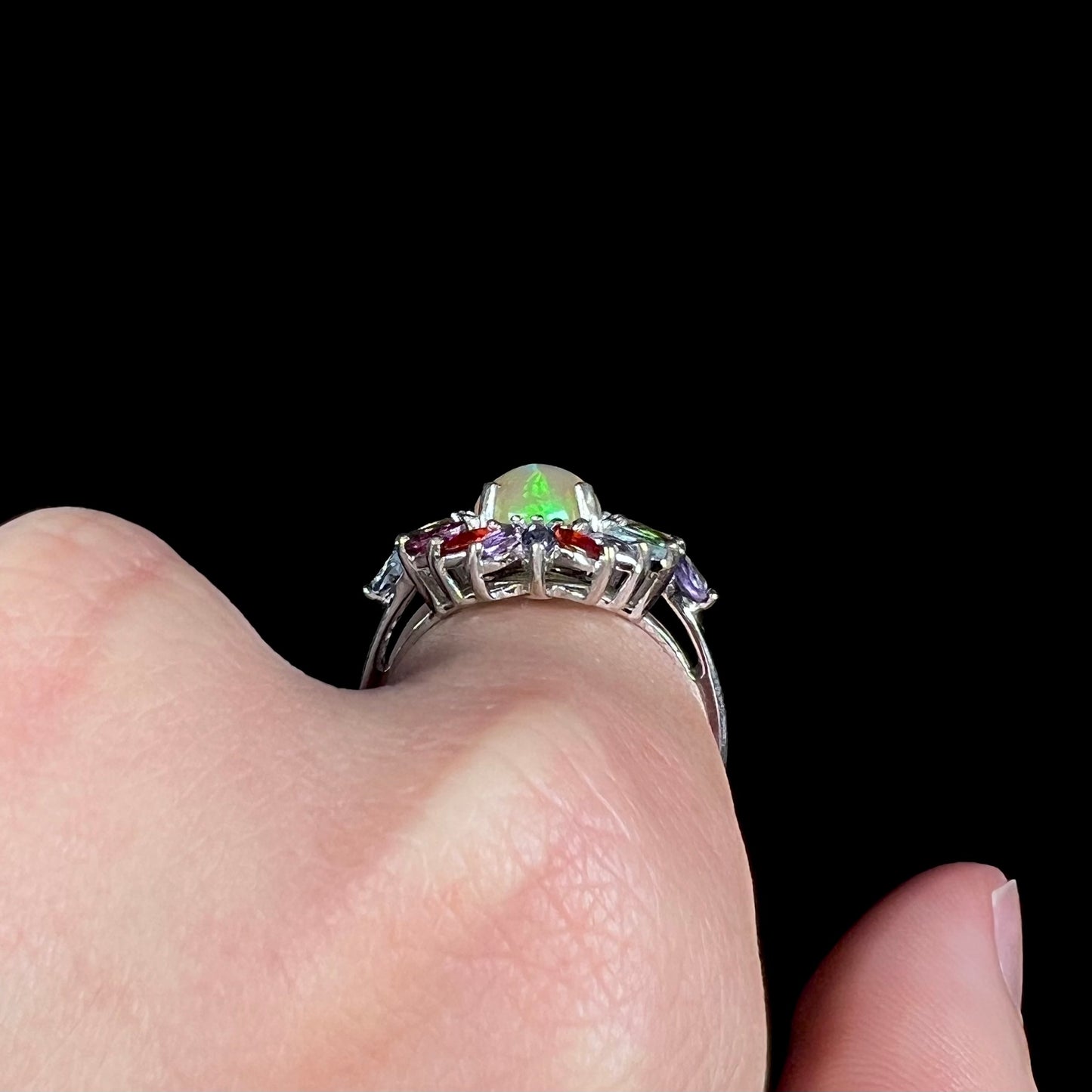Side profile view of a sterling silver opal gemstone ring worn on a finger against a black background.