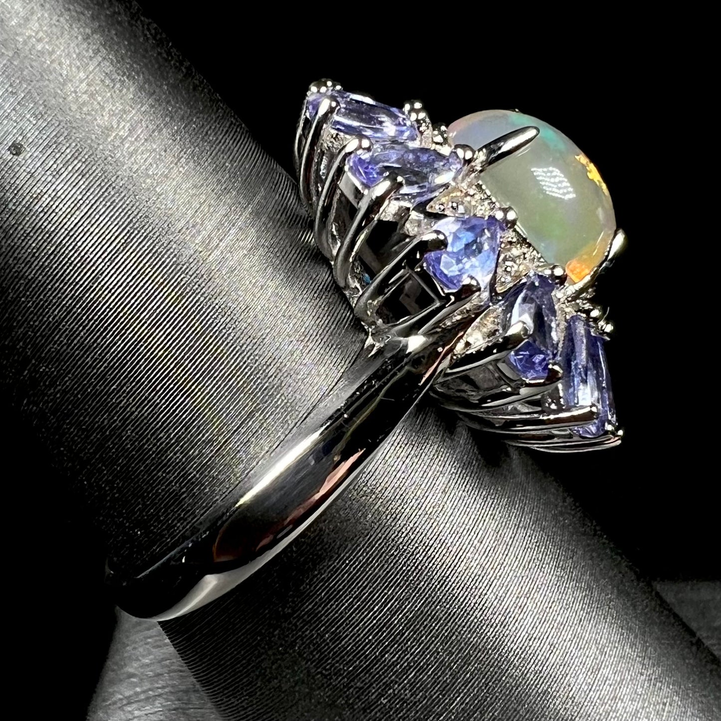 Side view of a silver opal tanzanite ring, focusing on the ring's metal shank, shown in LED light against black.