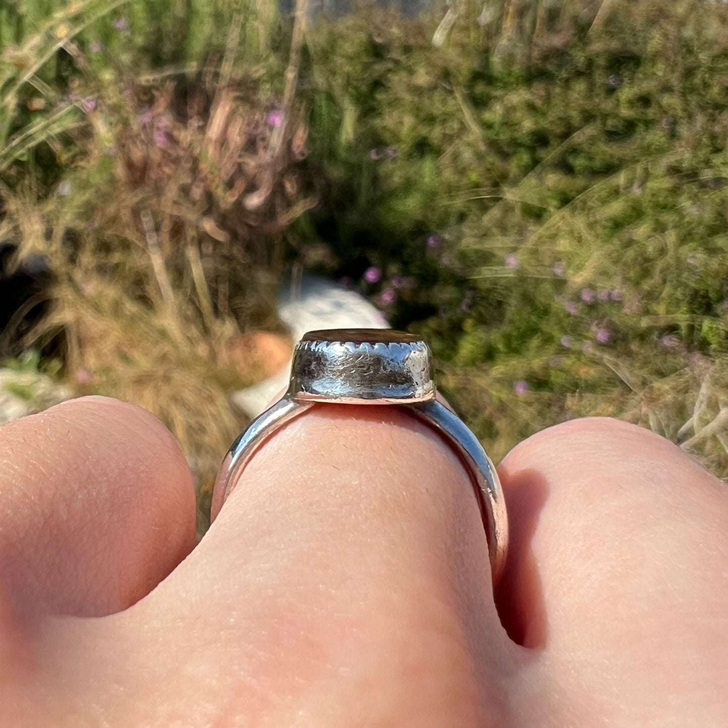 Silver bezel ring worn on a finger in sunlight showing the side gallery profile.