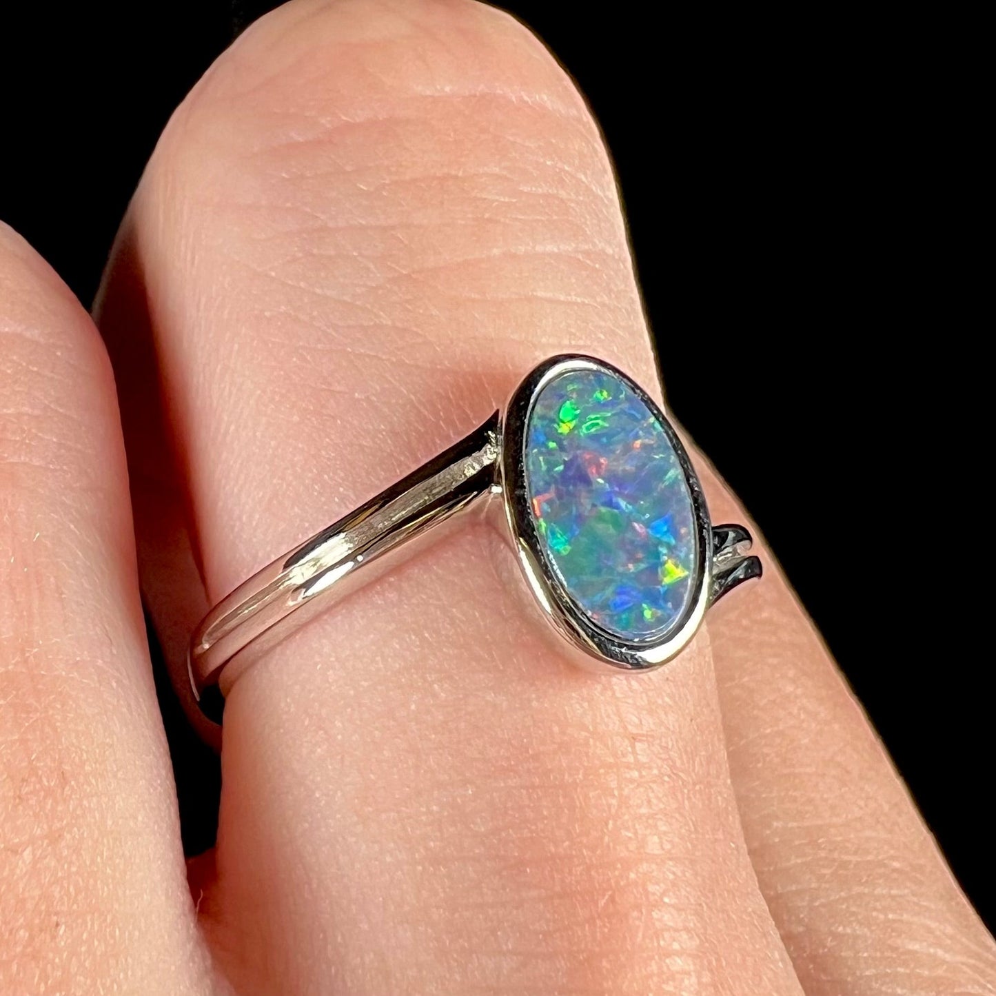 A sterling silver ring bezel-set with an oval shaped black opal doublet. The opal has red and blue fire.