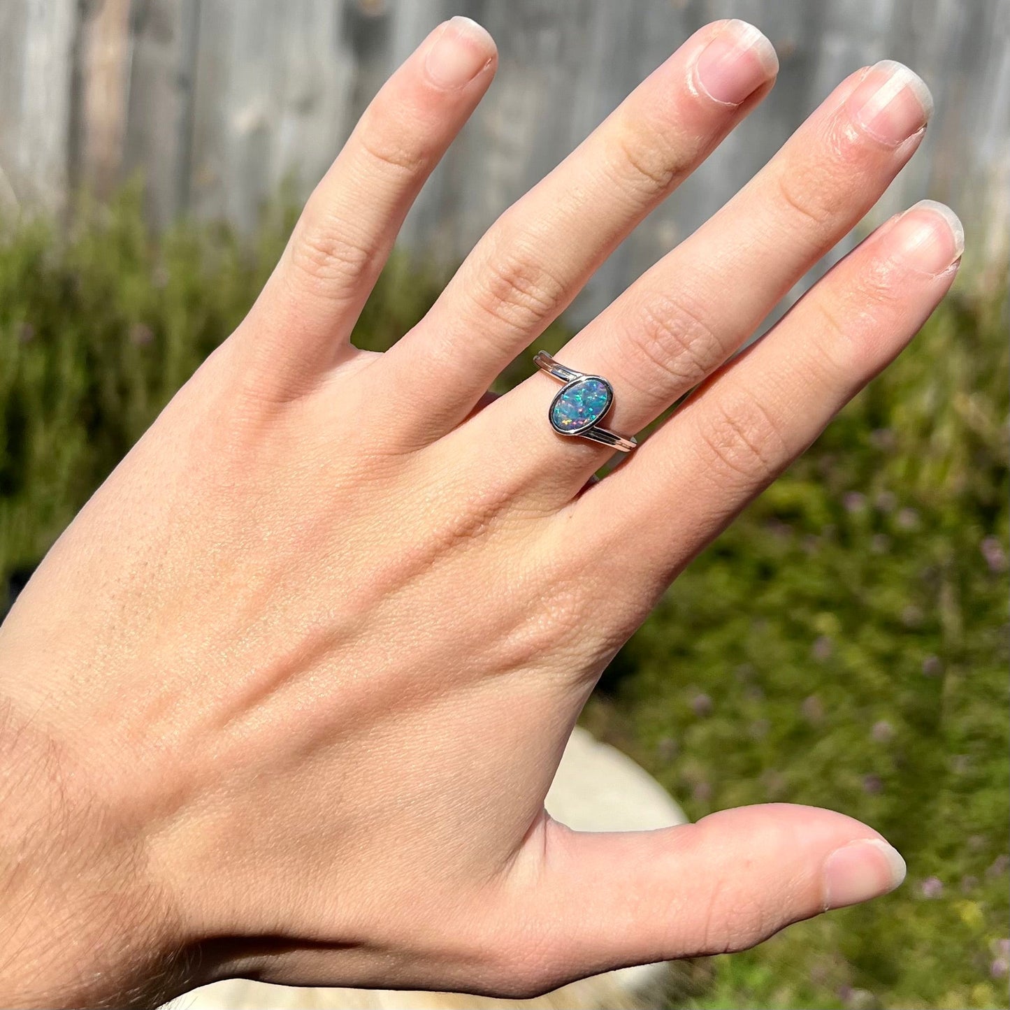 A sterling silver ring bezel-set with an oval shaped black opal doublet. The opal has red and blue fire.