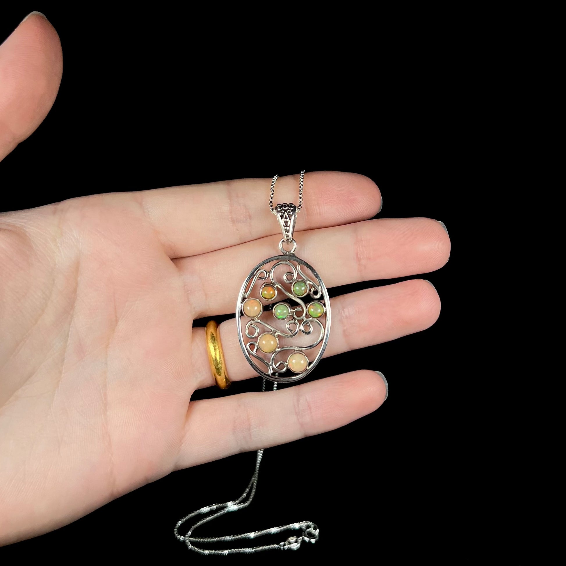 A sterling silver Boho-style Ethiopian opal necklace, shown in a hand against a black backdrop.