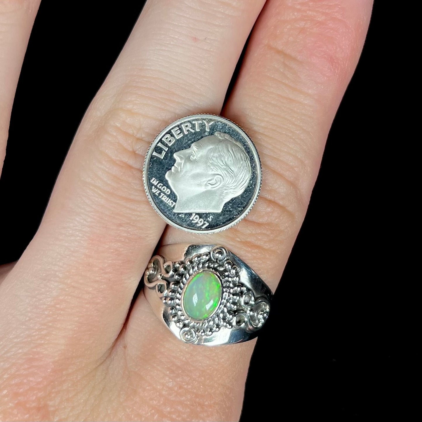 A silver boho-style opal ring worn on an index finger next to a 1997 S dime coin for scale.
