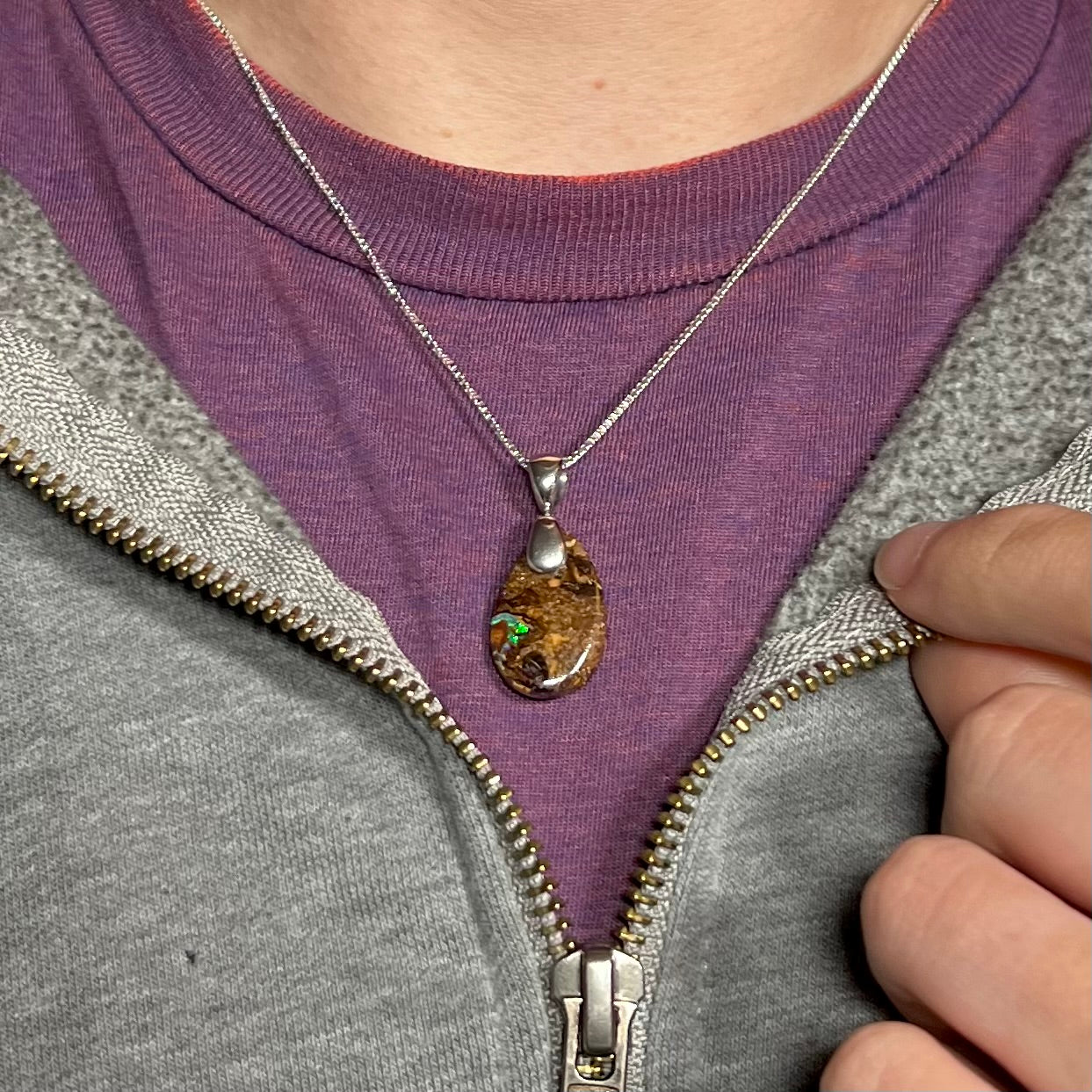 An Australian boulder opal necklace with a sterling silver bail, worn around a neck against a purple shirt.