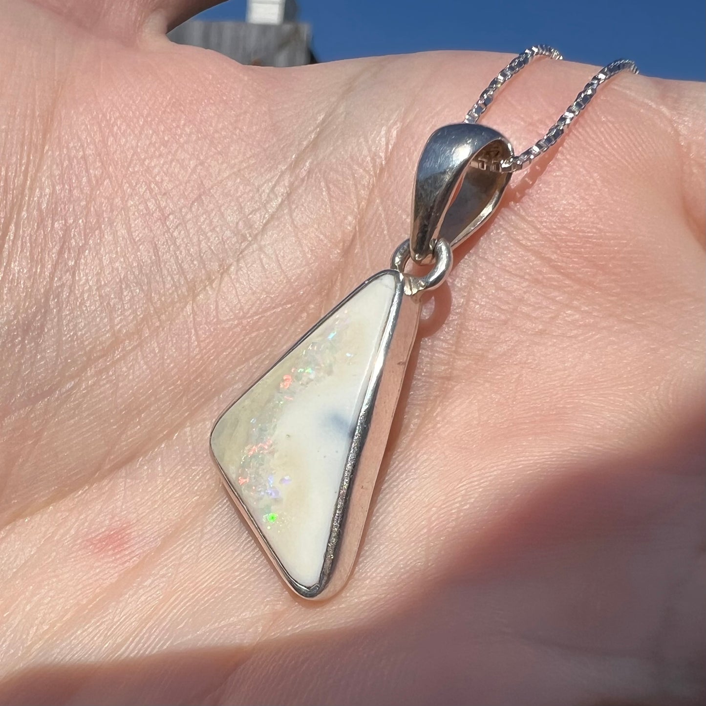 A white Australian boulder opal necklace in .950 silver, shown close-up at an angle in sunlight.