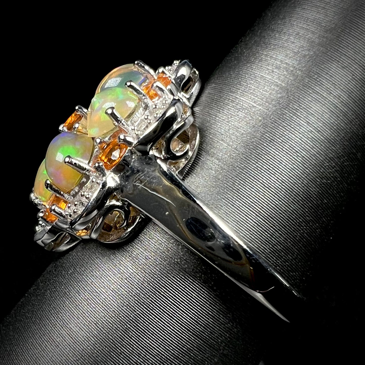 Side view of a silver opal cluster ring against a black background. A scratch can be seen in the ring's shank.
