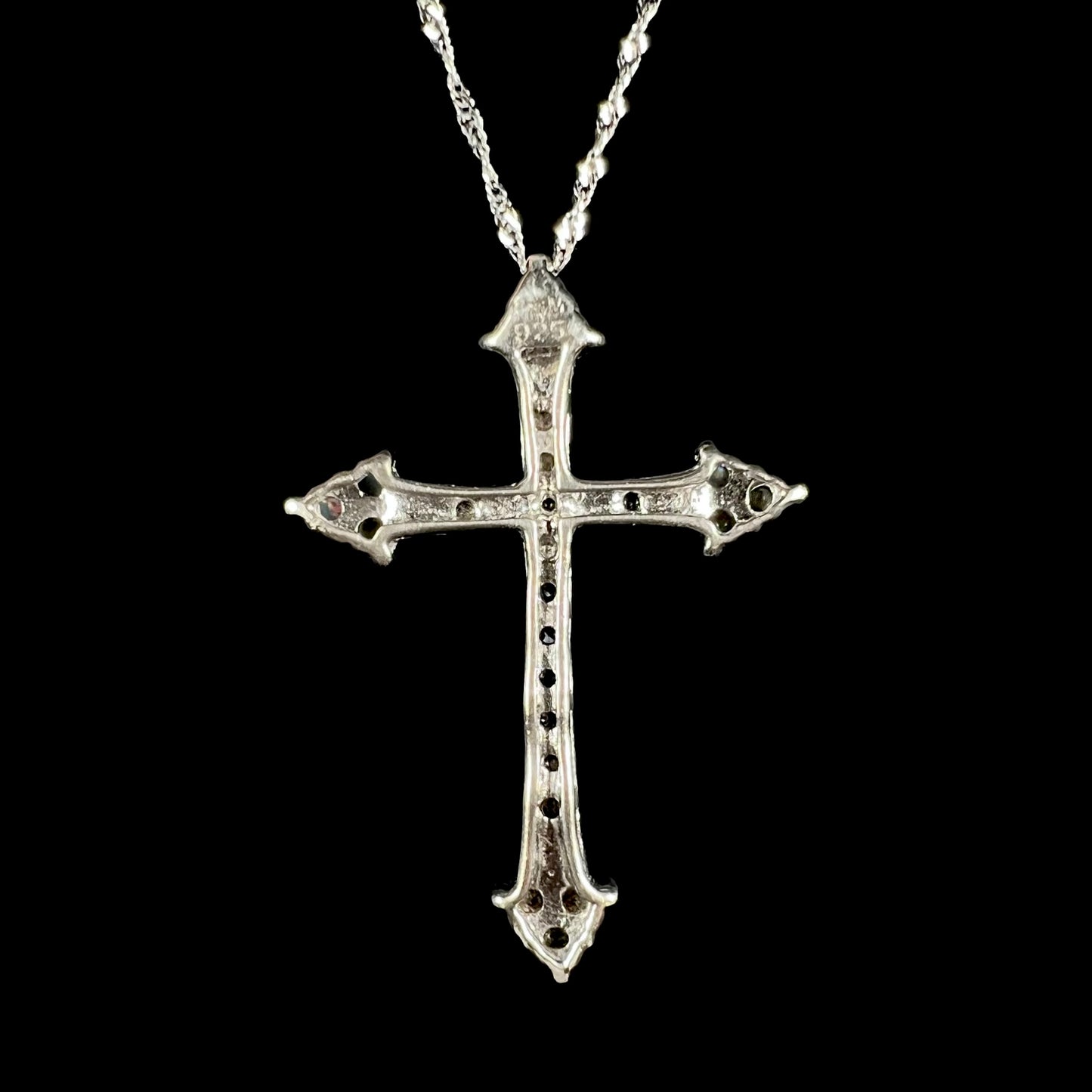 Back view of a silver cross necklace against a black backdrop.
