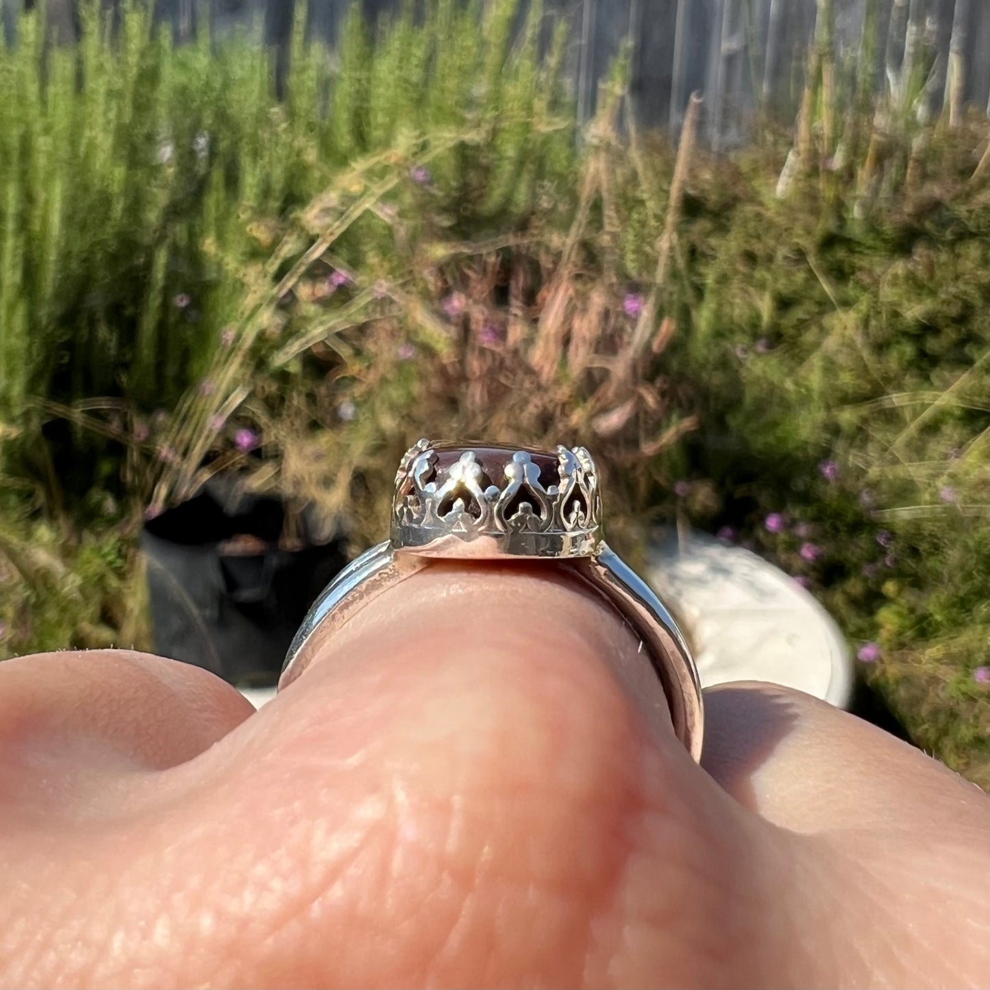 Side profile view of a silver crown motif ring, worn on a finger in sunlight.