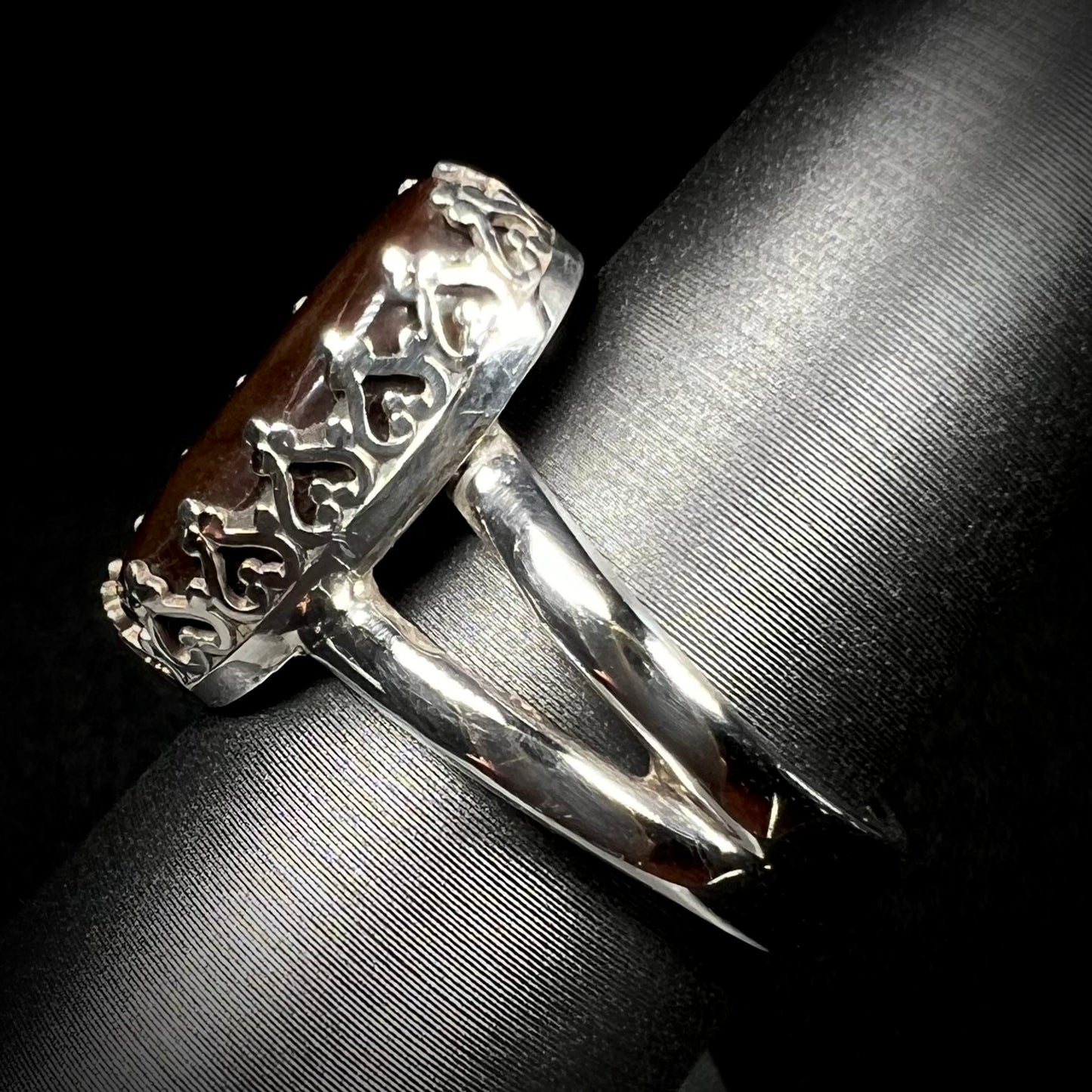 A sterling silver split shank ring with crown-design prongs shown from the side against dark backdrop.