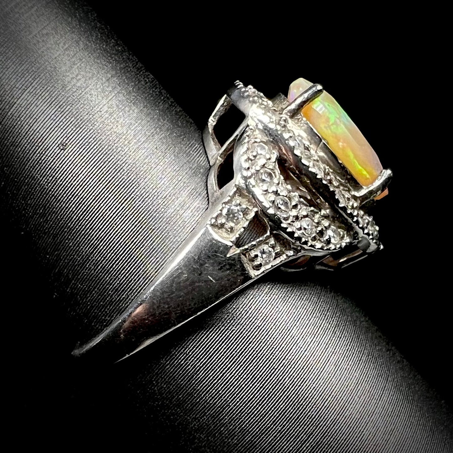 Side view of a silver CZ opal ring, the ring's shank in focus. Slight wear can be seen in the surface of the metal.