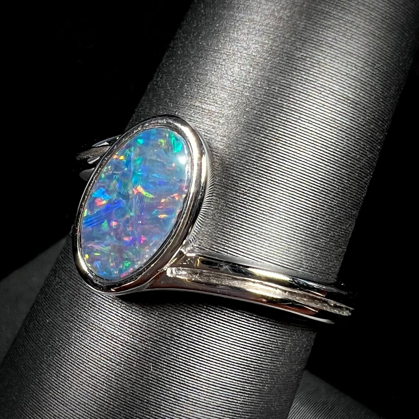 A sterling silver ring bezel-set with an oval shaped black opal doublet. The opal has red and blue fire.