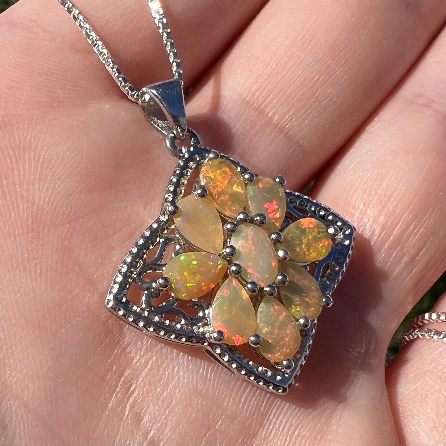 Angled view of a sterling silver Ethiopian opal cluster necklace, held in a hand in the sunlight.