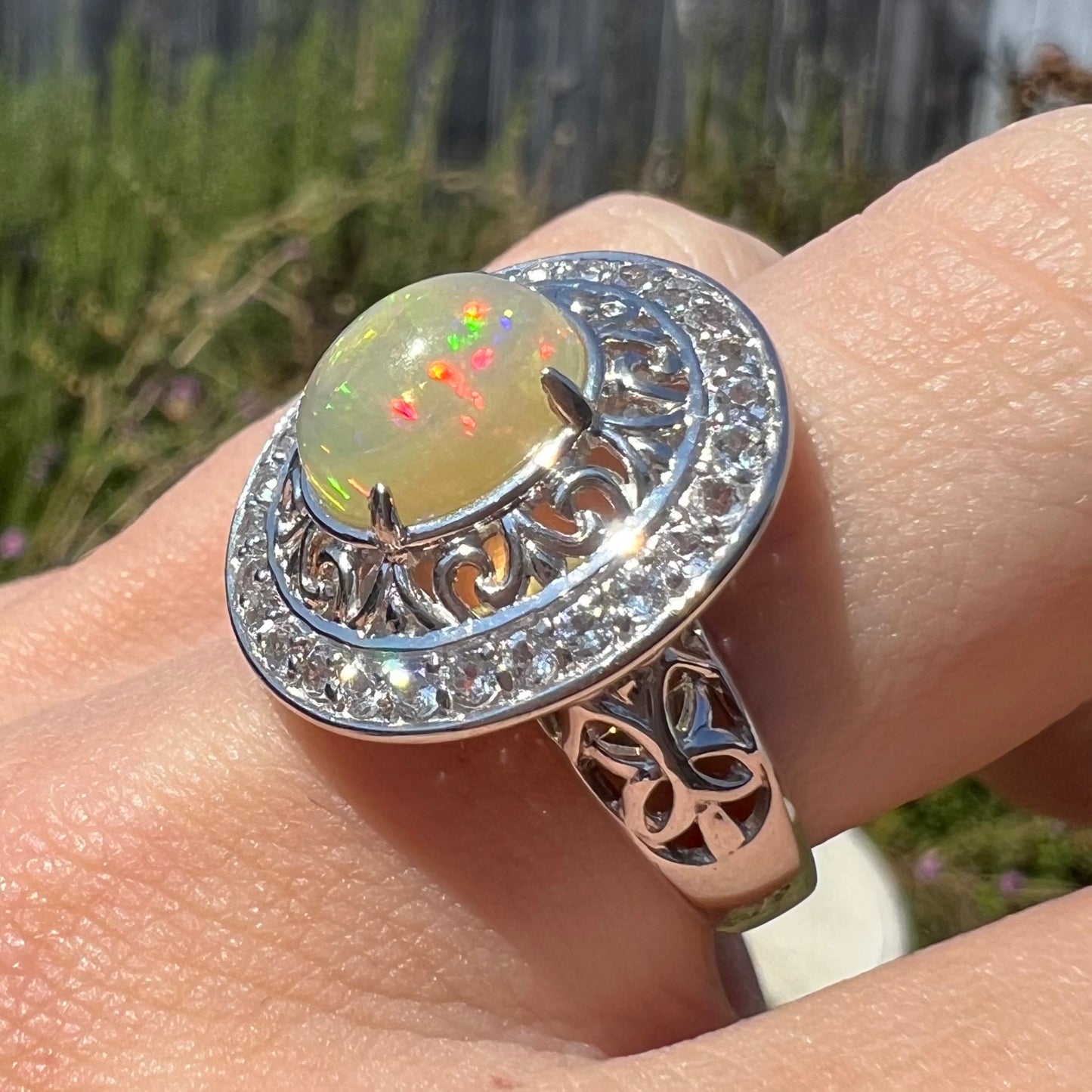 Close-up of a silver Ethiopian opal filigree ring worn on a finger in the sunlight.