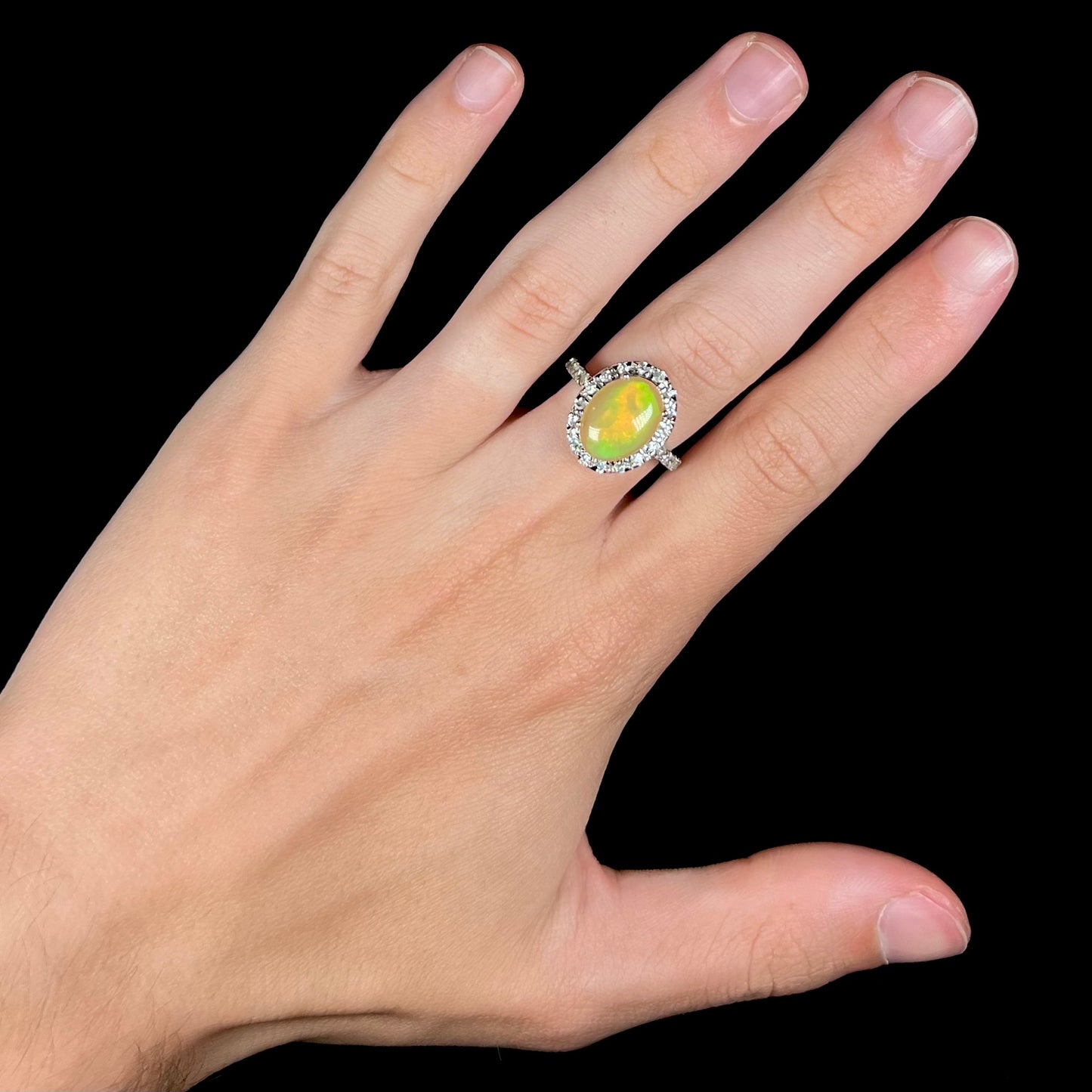 A sterling silver Ethiopian fire opal ring with a CZ halo worn on a hand against a black background.