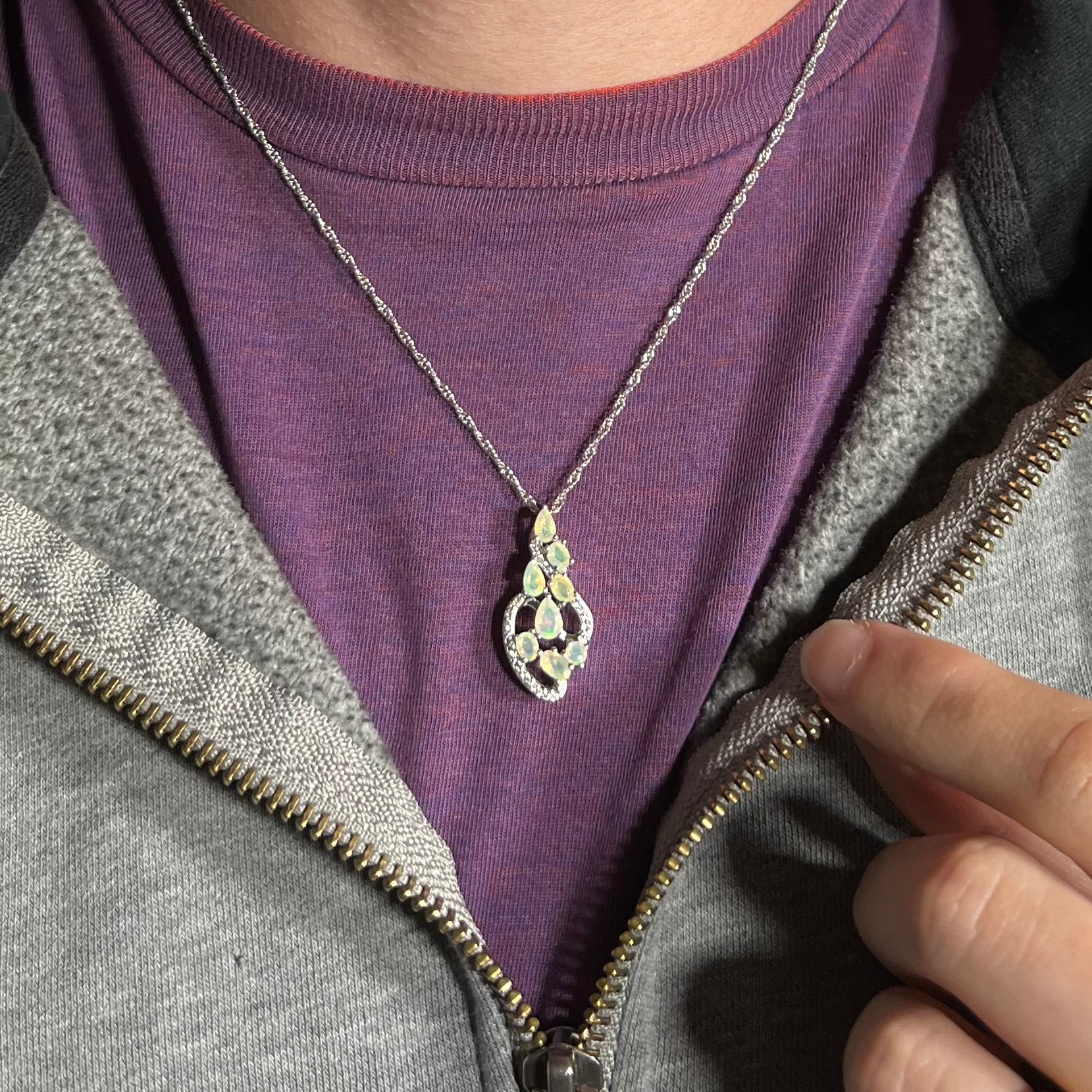 A sterling silver Ethiopian opal and CZ necklace worn around a neck against a purple shirt.