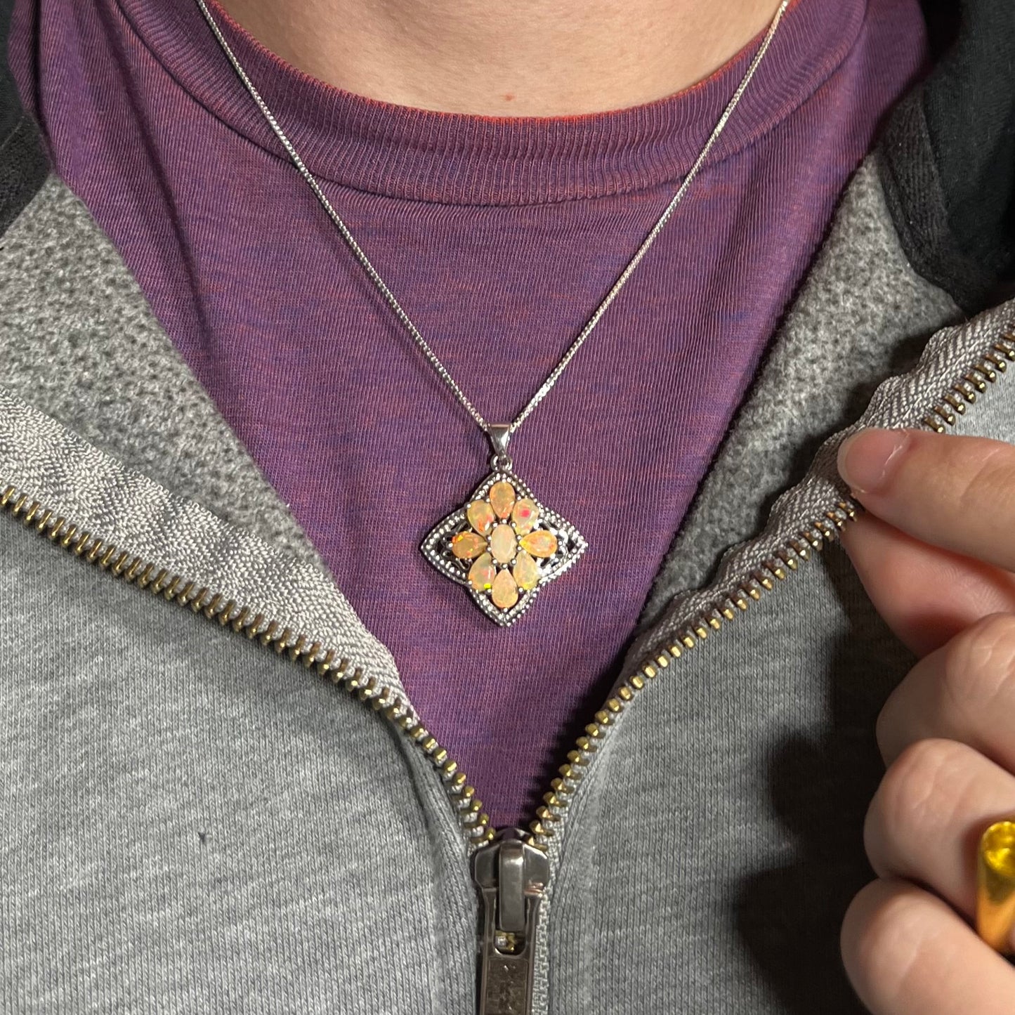 A sterling silver Ethiopian opal necklace worn around a person's neck against a purple shirt.