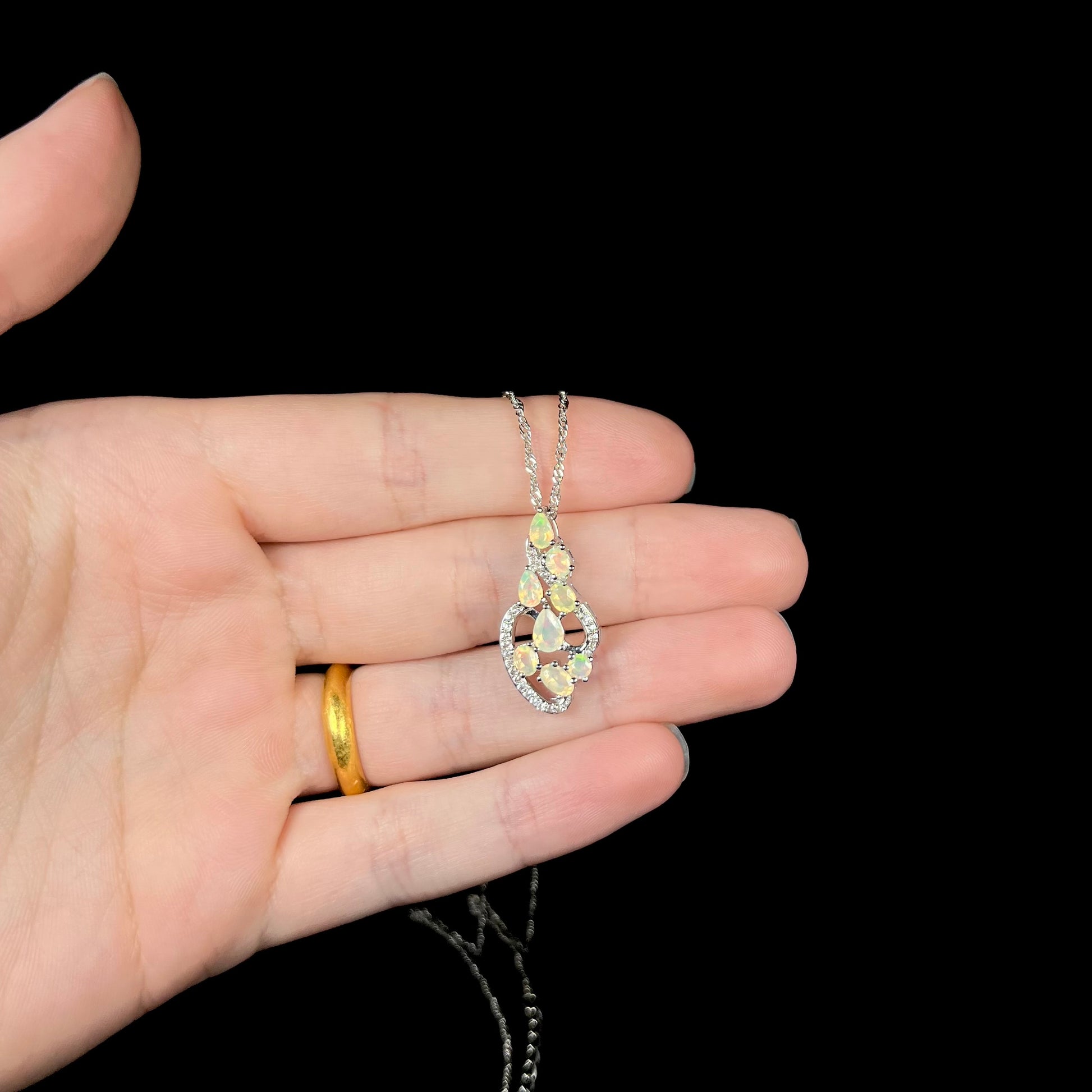 A sterling silver Ethiopian opal necklace shown resting in a hand under studio LED lighting against a black backdrop.