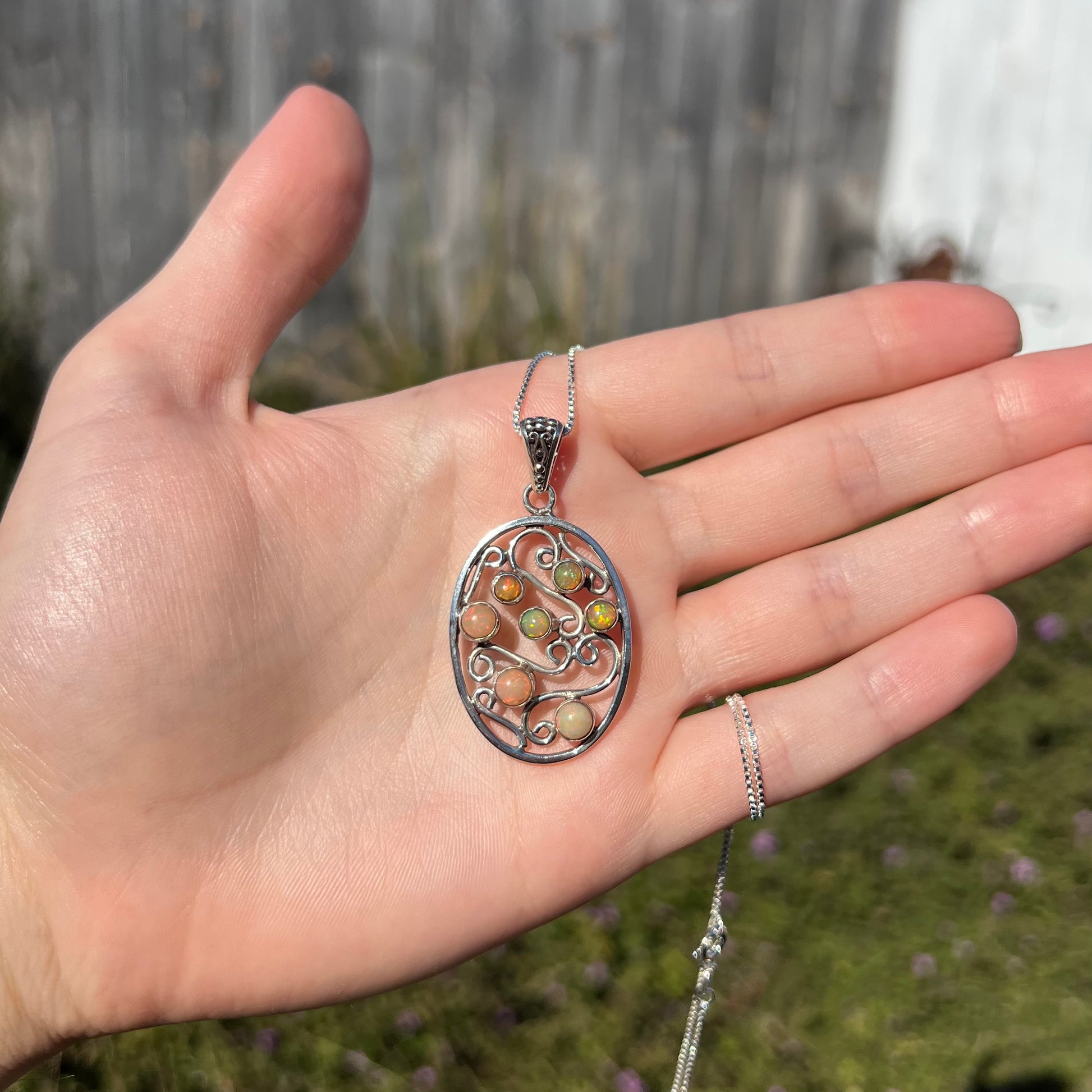 A sterling silver Ethiopian opal filigree necklace shown in a hand in sunlight.