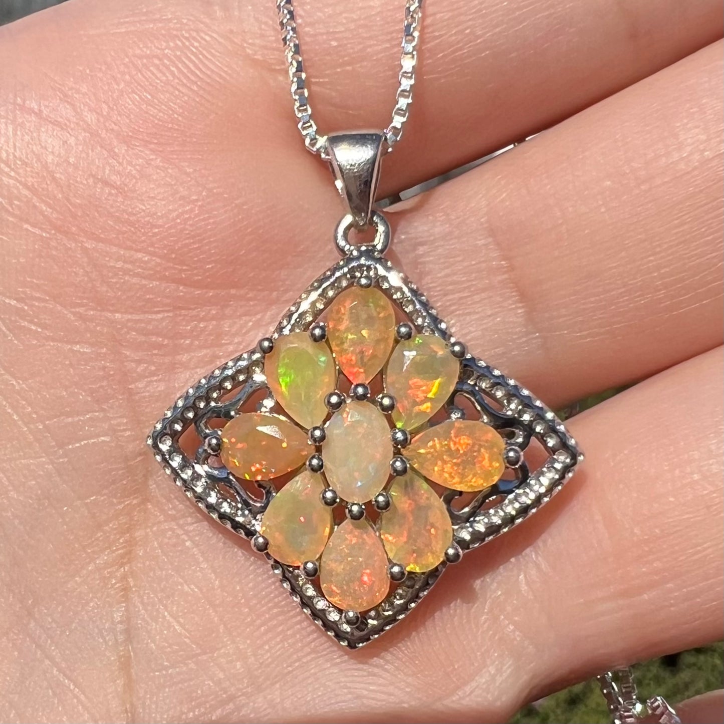A sterling silver Ethiopian opal necklace shown close-up in the sunlight, held in a hand.  The opals are orange and green.