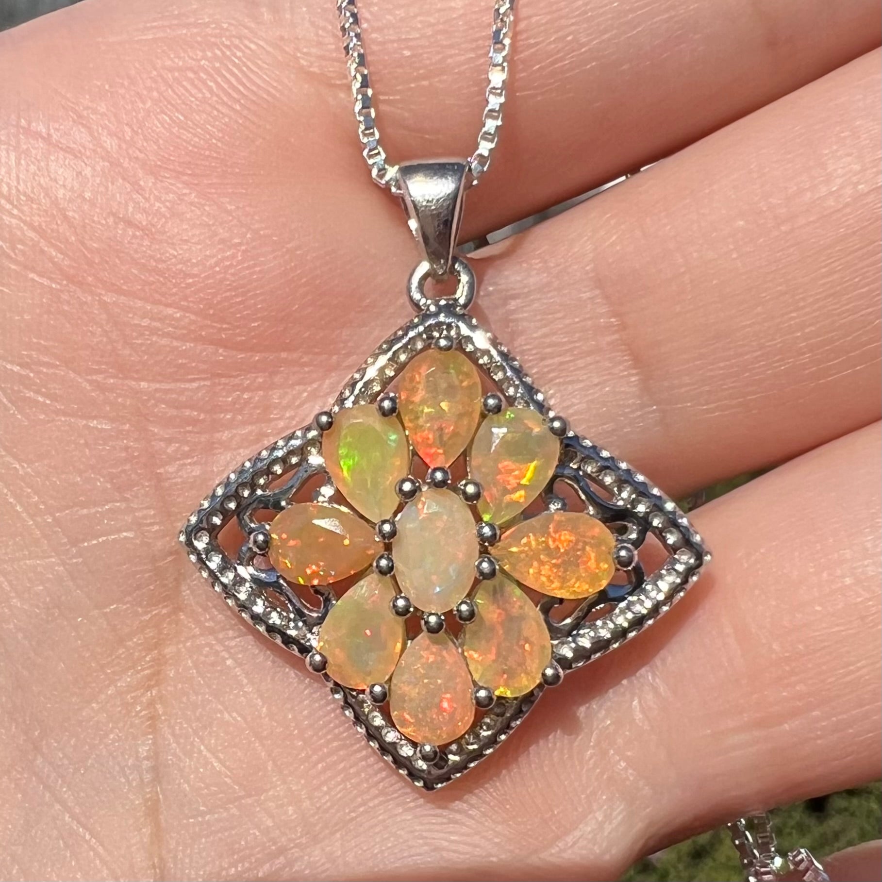 A sterling silver Ethiopian opal necklace shown close-up in the sunlight, held in a hand.  The opals are orange and green.